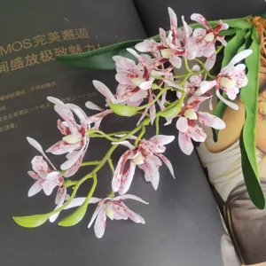 Closeup detail shot of artificial orchid branch featuring spotted petals and green leaves for decor.