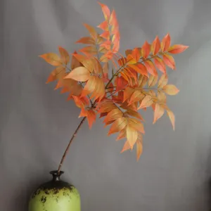 Primer plano detallado de rama de hojas de otoño artificiales con follaje naranja brillante.