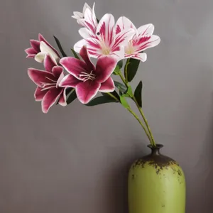 Vista dettagliata di gigli artificiali, petali viola e bianchi con foglie verdi.