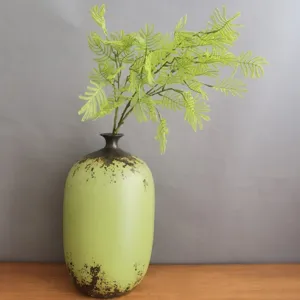 Detailed view of artificial green fern leaves bouquet in a vintage ceramic vase for decor.