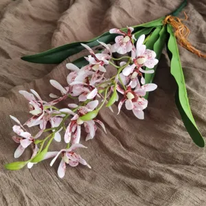 Artificial orchid flower branch detail shot, realistic spotted petals and green leaves for home decor.