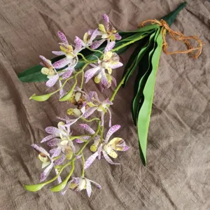 Artificial orchid flower detail shot, showing realistic petals and green leaves closely.