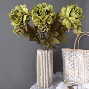Primo piano dettagliato di peonie artificiali verde vintage disposte in vaso di ceramica bianca.