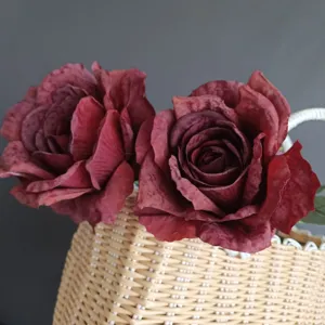 Primer plano de rosas artificiales vintage rojo oscuro con bordes quemados en cesta tejida.