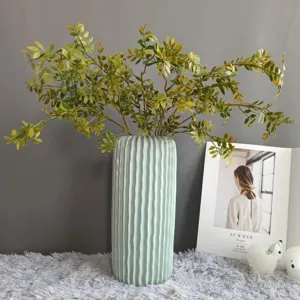 Vaso in ceramica decorativo con rami di fogliame artificiale, ideale per interni moderni.