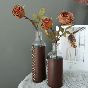 Vista detallada de florero de vidrio decorativo con funda de cuero y rosas artificiales.