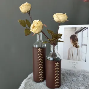 Vista detallada del florero de vidrio envuelto en cuero marrón con rosas amarillas artificiales.