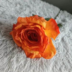 Vista detallada de flor artificial rosa naranja con bordes quemados para decoración del hogar.