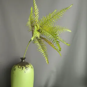 Artificial fern plant single branch detail view with green vase for home decor interior.