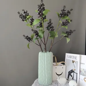 Artificial berry branches detail shot, dark purple foam fruits in ribbed light green vase for home decor.