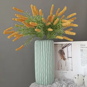 Detailansicht eines künstlichen gelben Salbeiblumenstraußes in einer grünen Keramikvase.