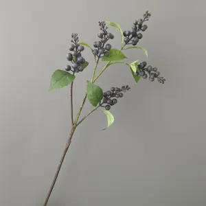 Artificial berry branch detail shot, dark purple fake fruit and green leaves for home decor.