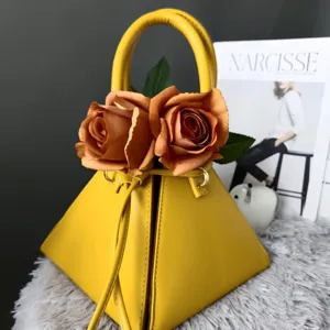 Primer plano de un bolso de mano triangular de cuero amarillo decorado con rosas artificiales.