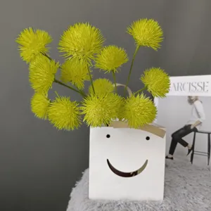 Artificial yellow dahlia fluffy ball flower set in white smiley container, close-up view detail.