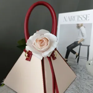 Elegante bolso de mano geométrico con asa roja y decoración de rosa blanca.