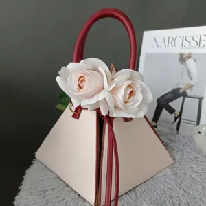 Bolso de mano piramidal geométrico en beige y rojo con flores de rosas blancas artificiales.