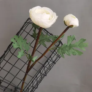 Artificial ranunculus flower detail shot, white peony fake flower head with green leaves stem.