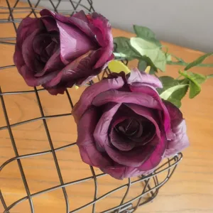 Gros plan détaillé de roses artificielles violettes foncées dans un panier en fil.