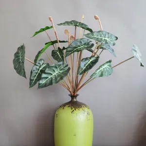 Detalle de planta artificial Alocasia oreja de elefante, hojas verdes con tallos en el jarrón.