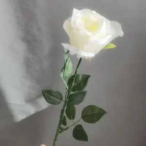 Gros plan de fleur de rose blanche artificielle, tige unique avec feuilles pour déco.