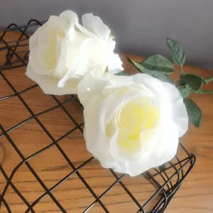 Gros plan détaillé de fleurs de roses blanches artificielles avec feuilles sur grille en métal.