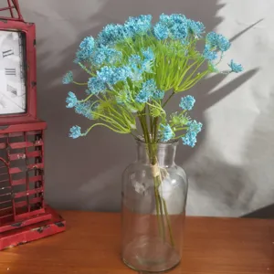 Close-up detail of blue artificial baby's breath flowers in a clear glass vase on wooden desk.