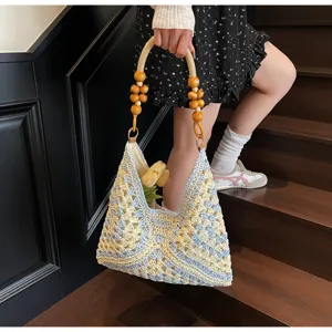Detailed view of handmade crochet straw shoulder bag with wooden bead handles, beach style.