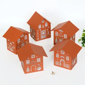 Detailed view of orange paper Christmas houses with white laser cut snowman and tree hollow designs.