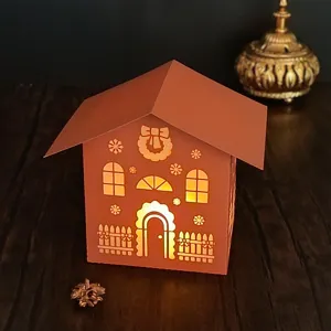 Christmas laser cut paper house night light detail, warm glowing holiday desktop decor prop.