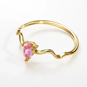 Detailed closeup of a golden wavy ring with a sparkling pear-shaped pink zirconia stone.