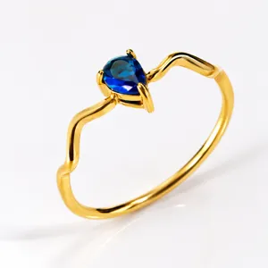 Detailed shot of a stylish minimalist wavy gold ring featuring a sparkling pear-cut blue zircon.
