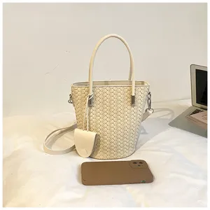 Vista dettagliata di una elegante borsa secchiello beige intrecciata con manico e tracolla.