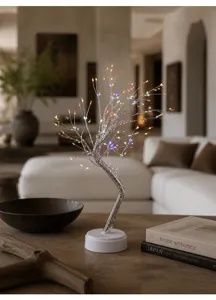 Nahaufnahme einer leuchtenden LED-Baumleuchte mit bunten Zweigen auf dem Holztisch.