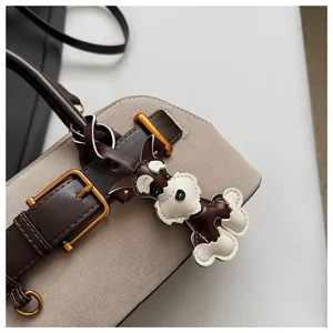 Nahaufnahme der Wildleder-Patchwork-Handtasche mit süßem Welpen-Anhänger und Metallschließe.