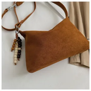 Brown suede underarm shoulder bag detail showing soft texture and chic wooden beaded pendant.