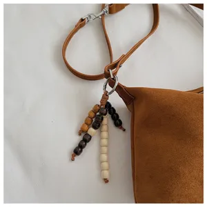 Brown suede underarm bag detail shot, featuring a wooden bead pendant and slim shoulder strap.