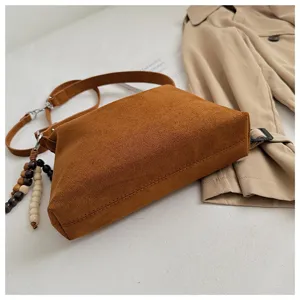 Brown suede shoulder bag detail view showing soft texture and chic wooden bead tassel pendant.