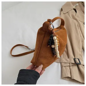 Brown suede underarm shoulder bag with chic wooden bead charm and minimalist pillow design.