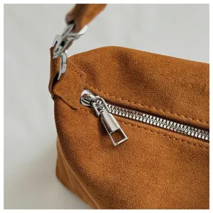 Close-up detail of brown suede shoulder bag showing metal zipper and hardware texture.