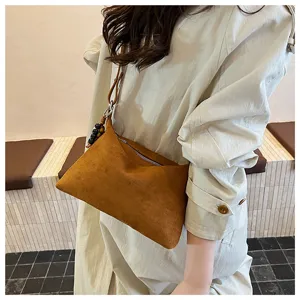 Brown suede underarm pillow bag detail view, soft shoulder strap and bead charm fashion style.