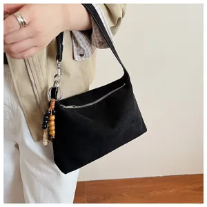 Black suede underarm shoulder bag detail showing soft fabric texture and wooden bead pendant charm.