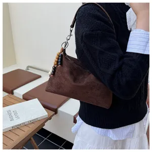 Detailed view of brown suede underarm shoulder bag featuring chic wooden bead pendant charm.