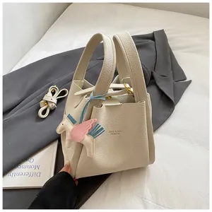 Close-up detail of stylish beige bucket handbag with cute pegasus charm and dual handles.