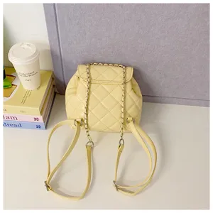 Detail shot of a yellow quilted mini backpack with chain straps on a clean tabletop setup.
