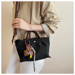 Close-up detail of stylish black nylon crossbody handbag with brown handles and chic heart charm.