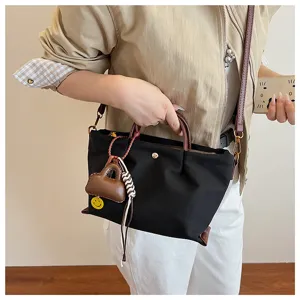 Detailed shot of black nylon handbag, versatile crossbody bag with brown handles and chic pendant.