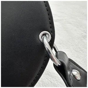 Detailansicht einer schwarzen Ledertasche mit glänzendem Metallring und feinen Nahtdetails.