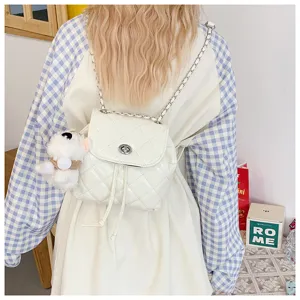 Detail shot of a white quilted mini backpack with metal chain straps and a cute plush dog charm.