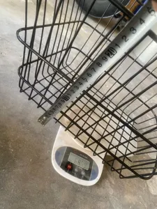 Detailed view of the black wire bicycle basket showing product dimensions and weight on scale.