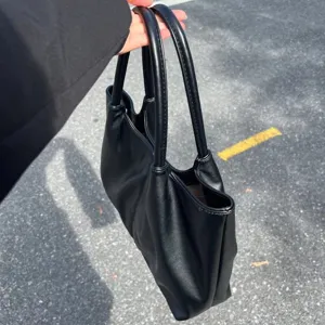 Minimalist solid black leather tote bag detail, featuring dual top handles and large capacity.